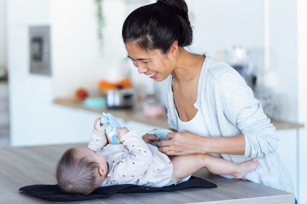 Colpo di giovane madre sorridente si diverte con il piccolo bambino mentre cambia il pannolino a casa.