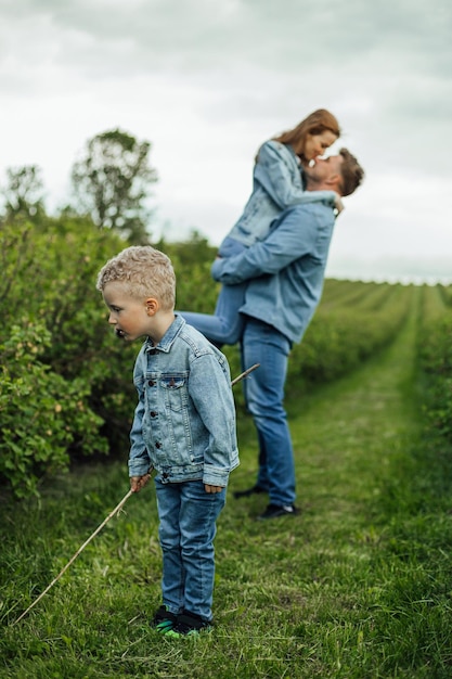 Colpo di piena crescita giovane famiglia in abiti casual denim che camminano per il parco tenendosi per mano in una calda giornata primaverile