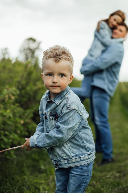 Colpo di piena crescita giovane famiglia in abiti casual denim che camminano per il parco tenendosi per mano in una calda giornata primaverile