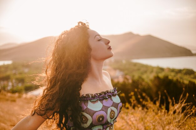 Colpo di stile di vita della donna dei capelli ricci che gode della luce del sole in estate