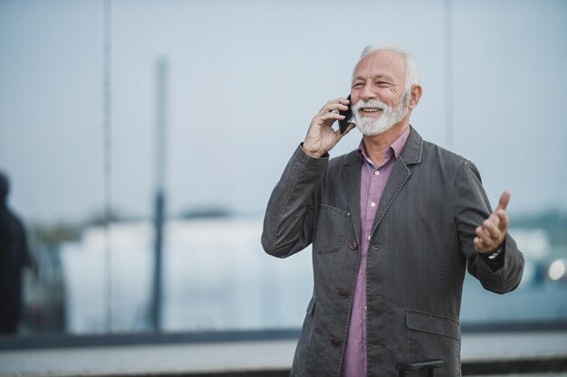 Colpo di un uomo d'affari senior di successo che parla su smart phone davanti a un edificio aziendale.