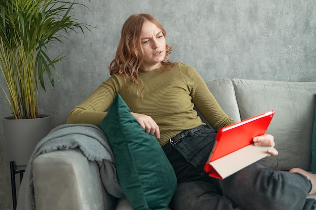 Colpo di una giovane donna triste che usa il suo tablet digitale per leggere mentre si siede sul divano di casa ciao