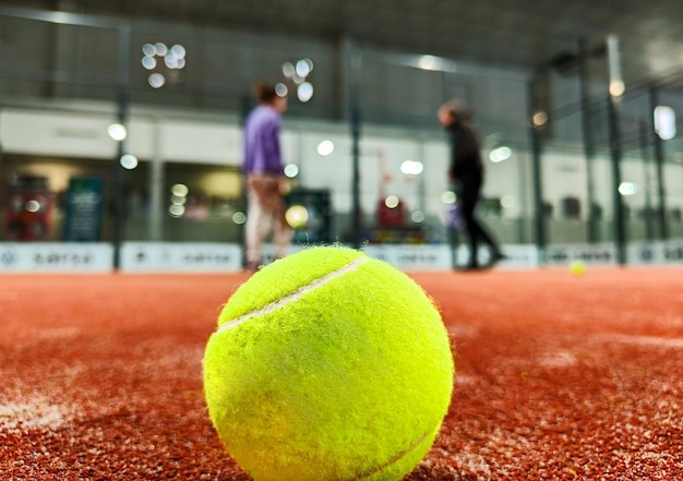 Colpo di una palla da paddle sul pavimento del campo da paddle tennis al coperto e tre amici giocatori