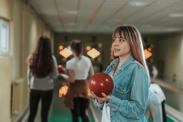 Colpo di una ragazza carina che tiene la palla da bowling al club di bowling.