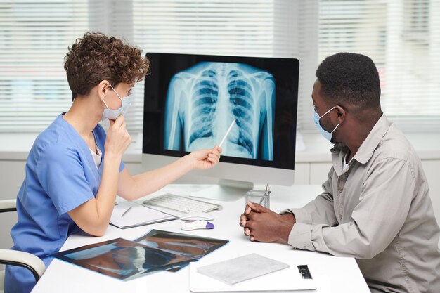 Colpo di vista laterale del pneumologo professionista che dimostra il colpo di raggi X al paziente sullo schermo del computer a