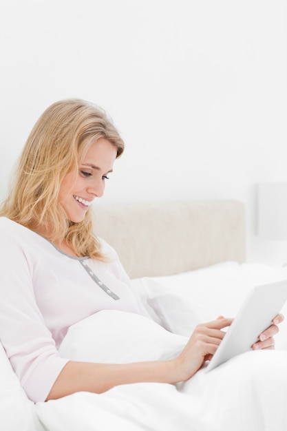 Colpo di vista laterale, donna a letto con tablet pc, guardando e sorridente