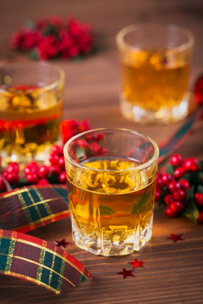 Colpo di whisky, brandy o liquore e decorazioni natalizie su fondo di legno. Concetto di vacanze stagionali. Avvicinamento