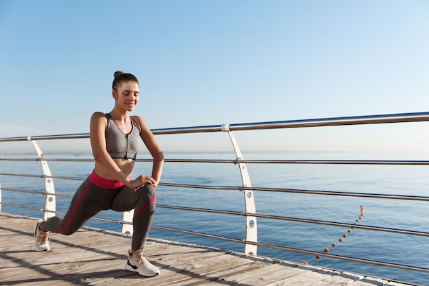 Colpo esterno della donna fitness attraente e sana formazione vicino al mare