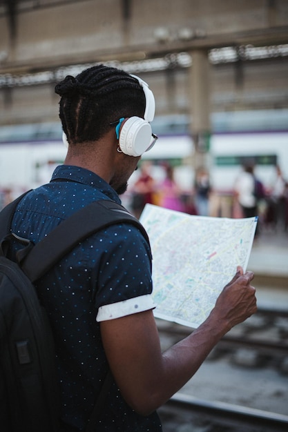 Colpo in prospettiva di un uomo africano che ascolta musica e guarda una mappa in una stazione ferroviaria