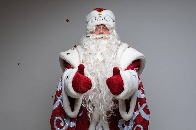 Colpo in testa di Babbo Natale in cappello rosso, uomo stanco barbuto dai capelli grigi su sfondo grigio studio. Foto di alta qualità