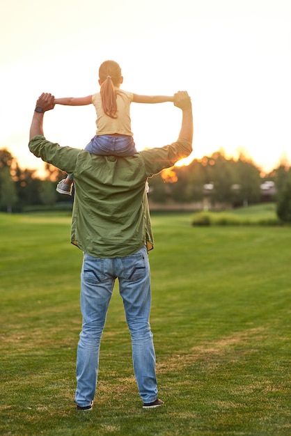 Colpo integrale della bambina seduta sulle spalle di suo padre mentre si godono il tramonto