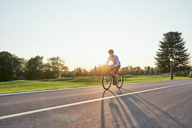 Colpo integrale di corridore maschio professionista in abbigliamento sportivo e allenamento casco in sella a una bici da strada