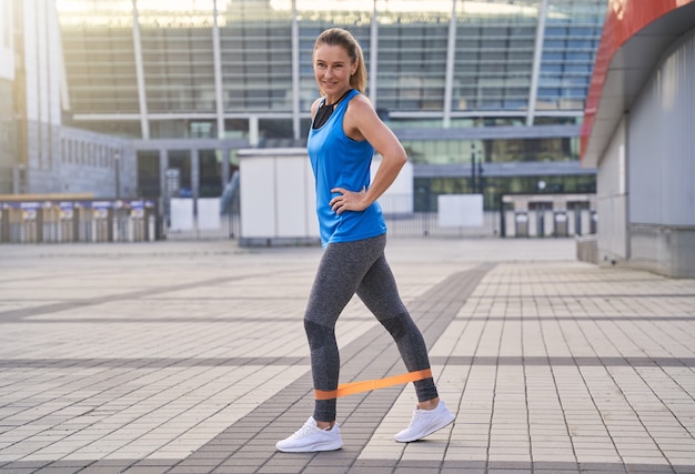 Colpo integrale di donna sportiva felice in abbigliamento sportivo che si scalda usando la fascia di resistenza mentre