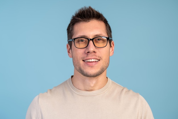 Colpo isolato di giovane bel maschio con barba e pettinatura alla moda, che indossa abiti casual in posa con un sorriso allegro in studio su sfondo blu