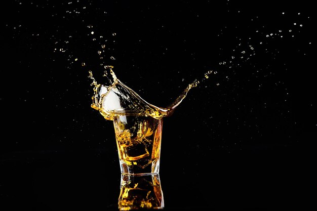 Colpo isolato di whisky con spruzzata su sfondo nero brandy in un bicchiere