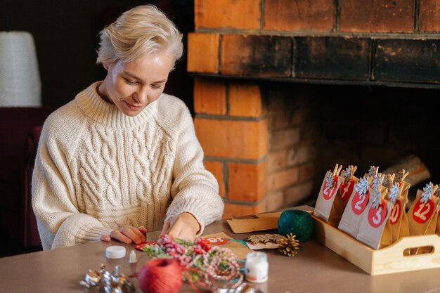 Colpo medio di una giovane donna che scrive il numero sulla borsa rossa che produce sacchetti di carta da carta kraft per il calendario dell'avvento alla vigilia di Natale seduti accanto al caminetto