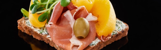 Colpo panoramico di prosciutto e pesche in scatola su panino smorrebrod danese su nero