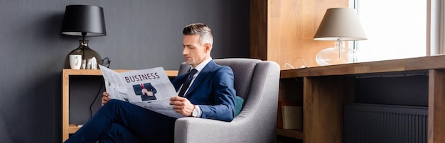Colpo panoramico di uomo d'affari in giacca e cravatta che legge il giornale con scritte aziendali