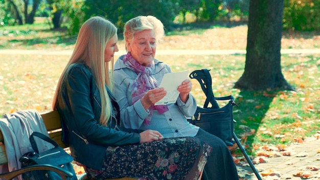 Colpo pieno della donna anziana che legge una lettera alla giovane donna graziosa in parco. Sta leggendo una storia interessante della sua vita.