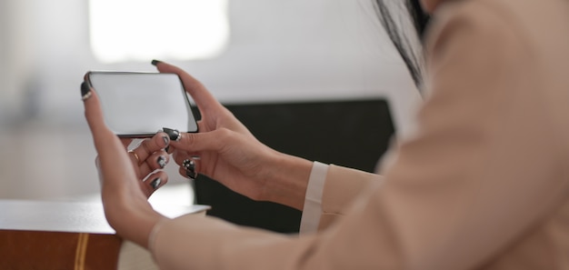 Colpo potato della donna di affari che utilizza smartphone del modello mentre lavorando al suo progetto nella stanza comoda dell'ufficio