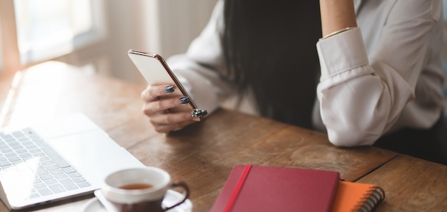 Colpo potato della donna di affari che utilizza smartphone mentre lavorando al suo progetto nella stanza comoda dell'ufficio