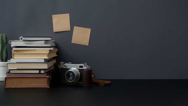 Colpo potato di area di lavoro con lo spazio, la macchina fotografica, i libri e le decorazioni della copia sulla tavola nera con la parete grigia