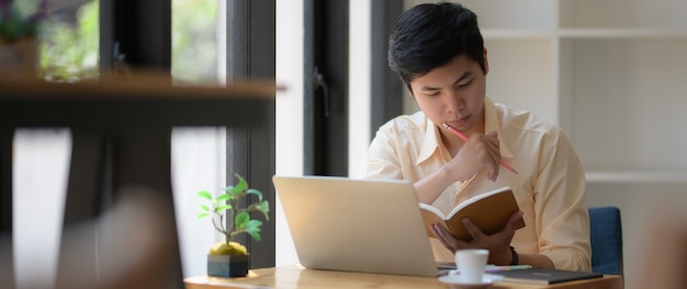 Colpo potato di giovane studente di college che si concentra sul libro e sul computer portatile