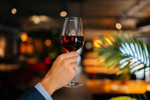 Colpo ritagliato del primo piano di un abito di moda elegante e irriconoscibile che tiene bicchieri di vino rosso nel ristorante con interni di lusso