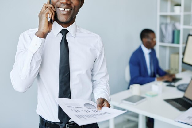 Colpo ritagliato di giovane uomo d'affari afroamericano che parla al telefono nello spazio della copia dell'ufficio