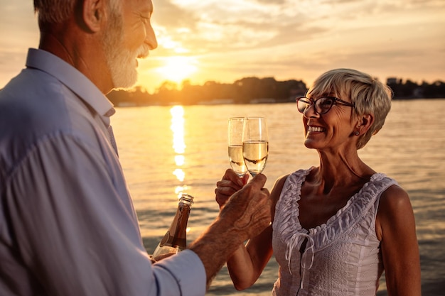 Colpo ritagliato di un'affettuosa coppia senior che brinda con champagne in riva al fiume Toni caldi