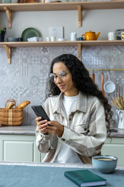 Colpo verticale bella donna ispanica che utilizza smartphone a casa donna con capelli ricci e occhiali