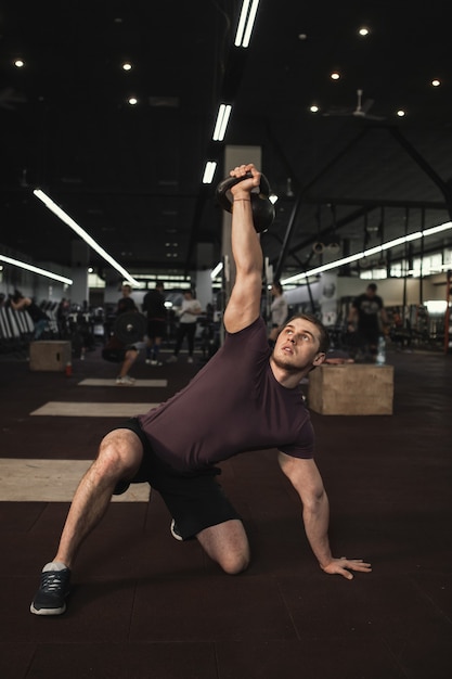 Colpo verticale di un atleta maschio muscoloso bello alzarsi con kettlebell turco