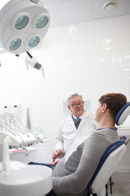 Colpo verticale di un dentista maschio anziano che ha appuntamento con il paziente presso la clinica