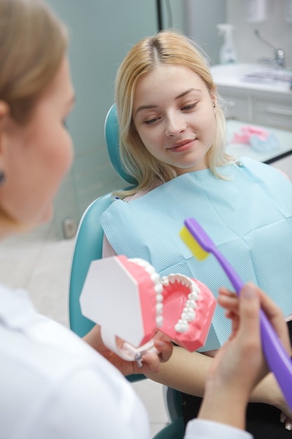 Colpo verticale di un paziente di sesso femminile seduto in poltrona odontoiatrica a parlare con il suo dentista