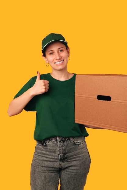 Colpo verticale di una consegna femminile che tiene una grande scatola e mostra il pollice in su