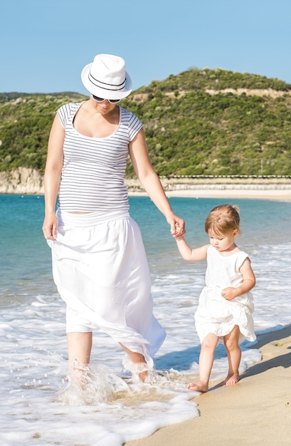 Colpo verticale di una madre caucasica che cammina sulla spiaggia con sua figlia durante la luce del giorno