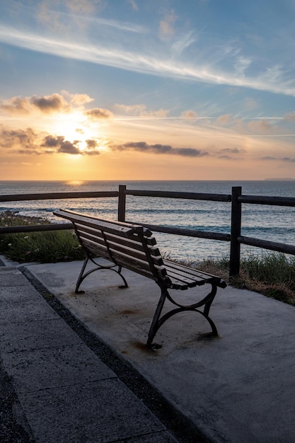 Colpo verticale di una panca di legno sulla spiaggia all'alba