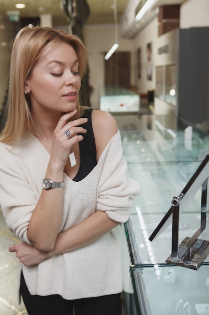 Colpo verticale di una splendida donna che prova gioielli presso il negozio