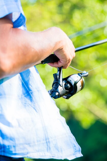 Colpo vicino del pescatore di sport che annaspa in linea sulla canna da pesca