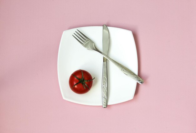 Coltello a forchetta e piatto bianco con pomodoro su sfondo rosa Piatto pulito e posate