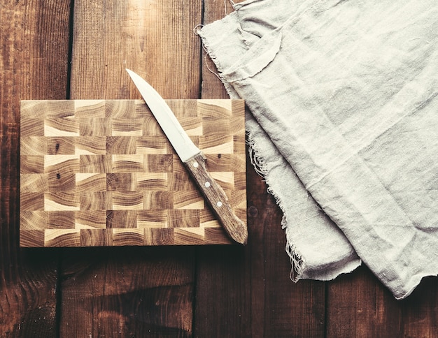 Coltello da cucina in metallo e tagliere di legno su un tavolo fatto di assi di legno marroni, vista dall'alto