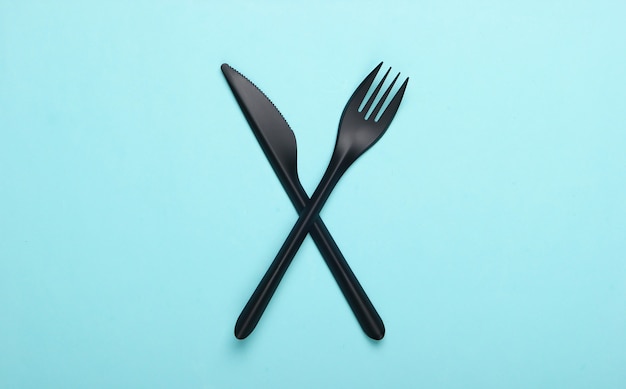 Coltello di plastica nera con una forchetta su una superficie blu