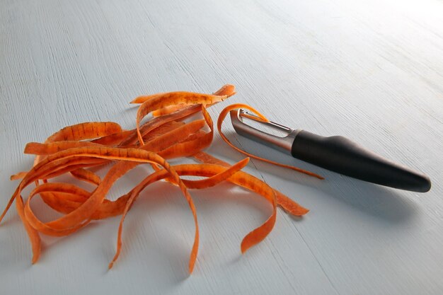 Coltello per sbucciare verdure e carote su un tavolo di legno leggero
