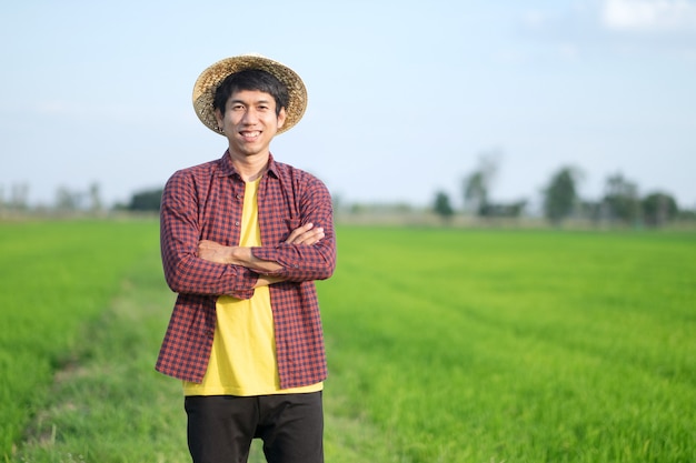Coltivatore asiatico uomo in piedi traverse di armi all'azienda agricola di riso verde