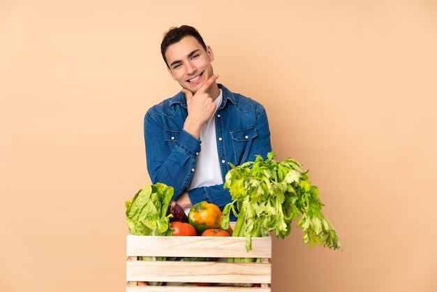 Coltivatore con le verdure appena raccolte in una scatola isolata sul sorridere beige della parete