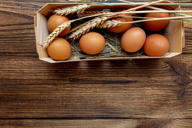 Coltivi le uova marroni con paglia in primo piano di legno del contenitore di betulla con lo spazio della copia