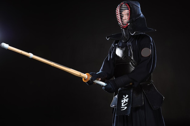 Combattente di Kendo in casco tradizionale che tiene la spada di bambù sul nero