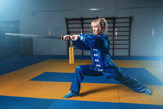 Combattente di wushu femminile con la spada in azione, arti marziali. La donna in posa blu del panno con la lama