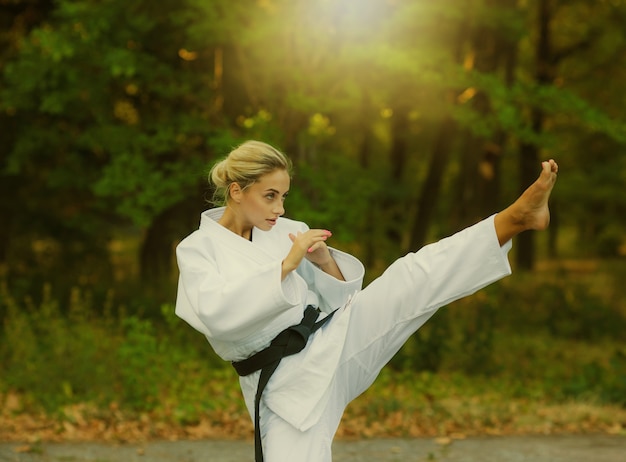 Combattente maestro femminile attraente in kimono bianco con cintura nera calci all'aperto Ã‚Â