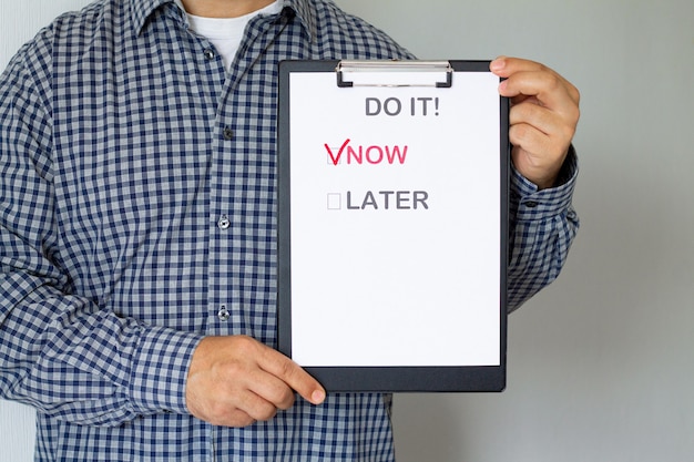 Combattere la procrastinazione e il concetto di business. Man holding poster di carta con il testo "Now or Later"